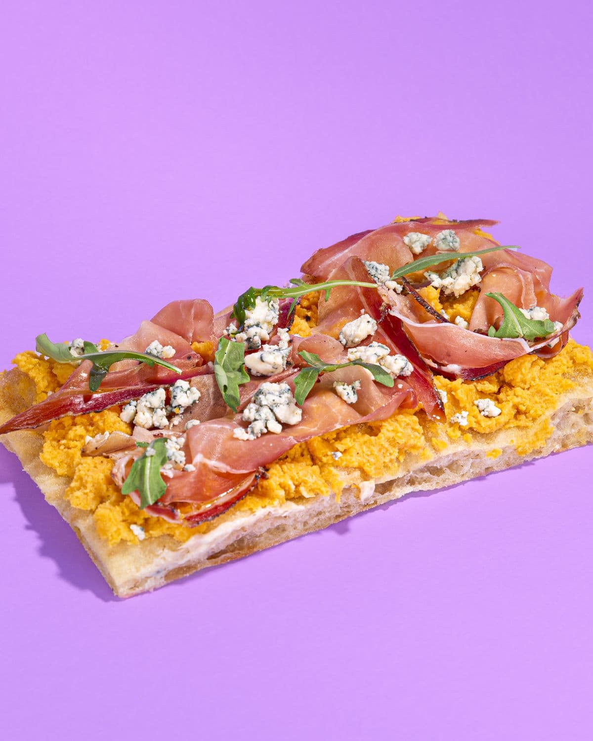 Trancio con prosciutto crudo, crema di zucca e rucola su fondo lilla